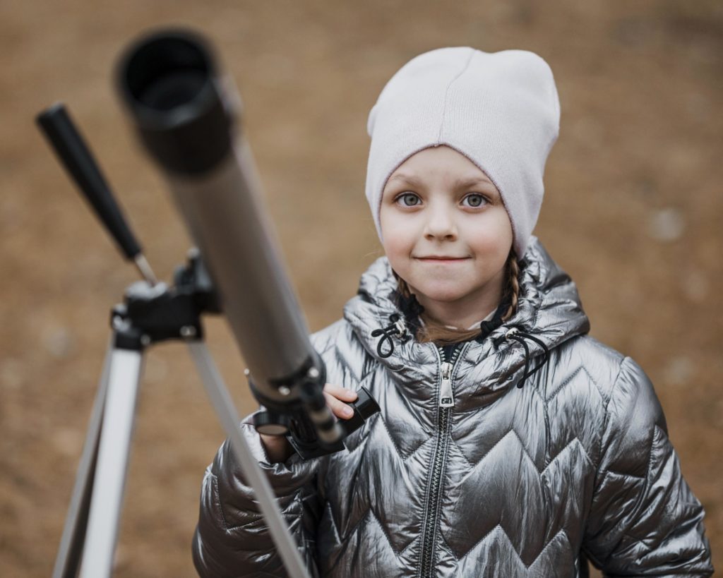 Astronomy for Kids: Girl smiling with a telescope. 