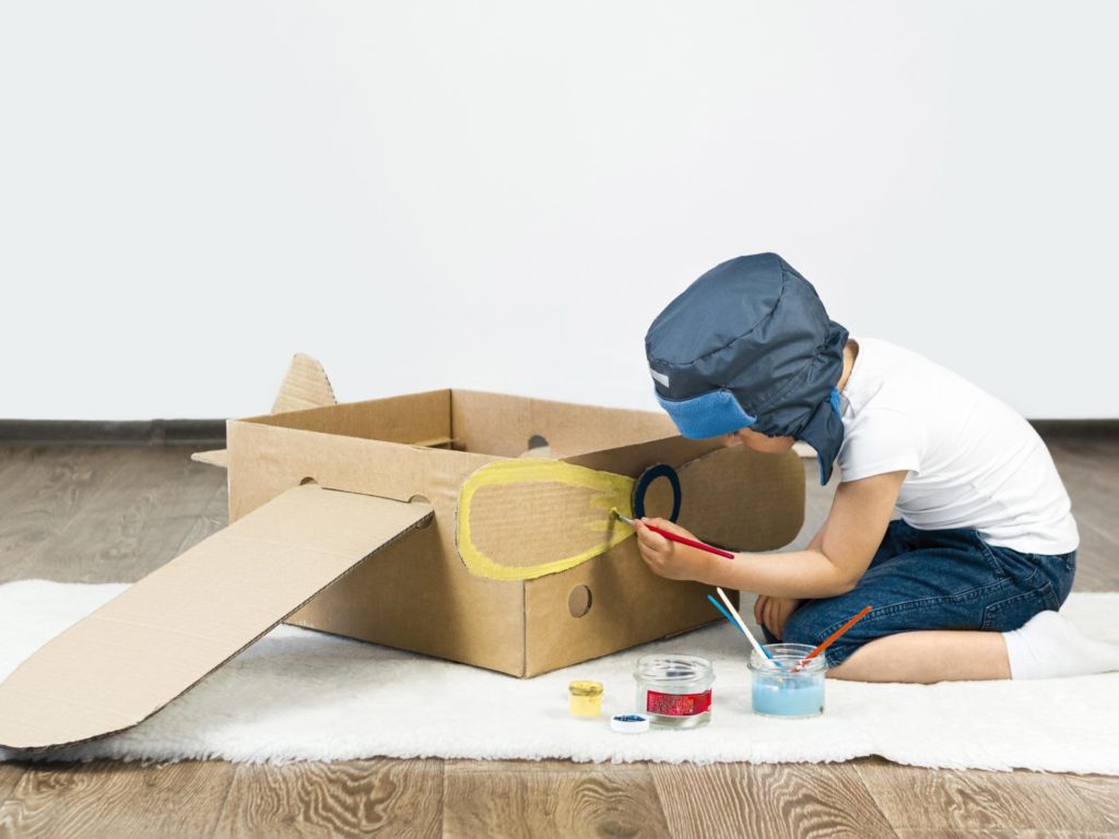 Child painting cardboard box airplane. 