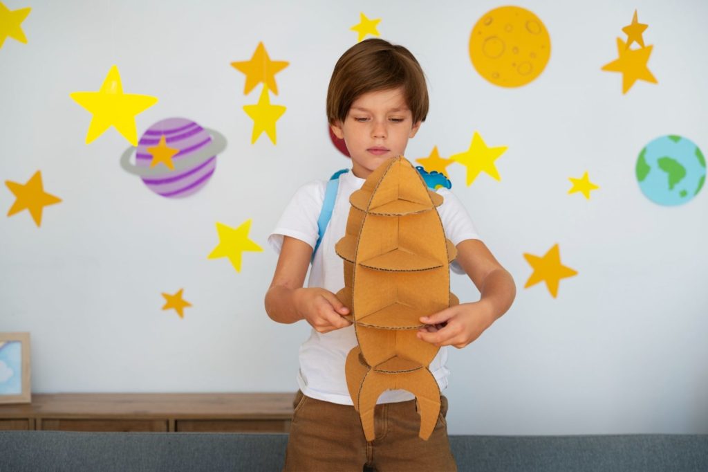 Astronomy toys for kids. Young boy playing with cardboard spaceship. 