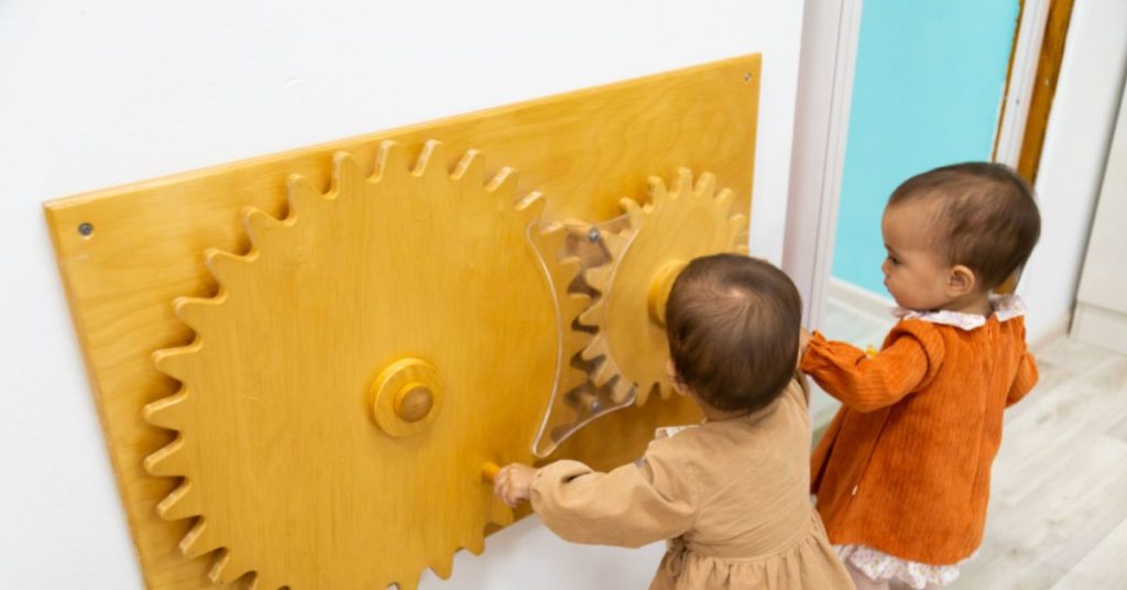 Two toddlers playing with wall gear activity.