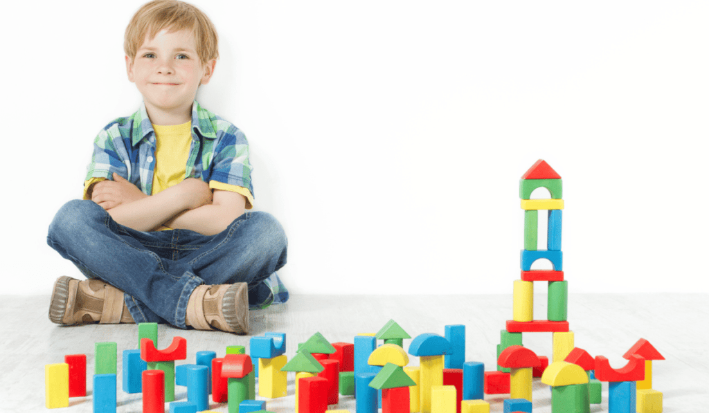 Image of boy smiling and sitting with building blocks. 